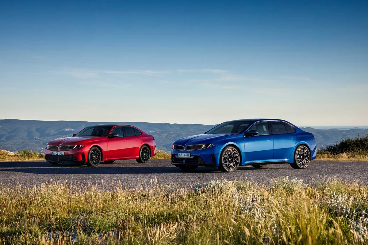 Two 2027 BMW 3 Series sedans, a red M350 xDrive and a blue model, parked on a mountain road