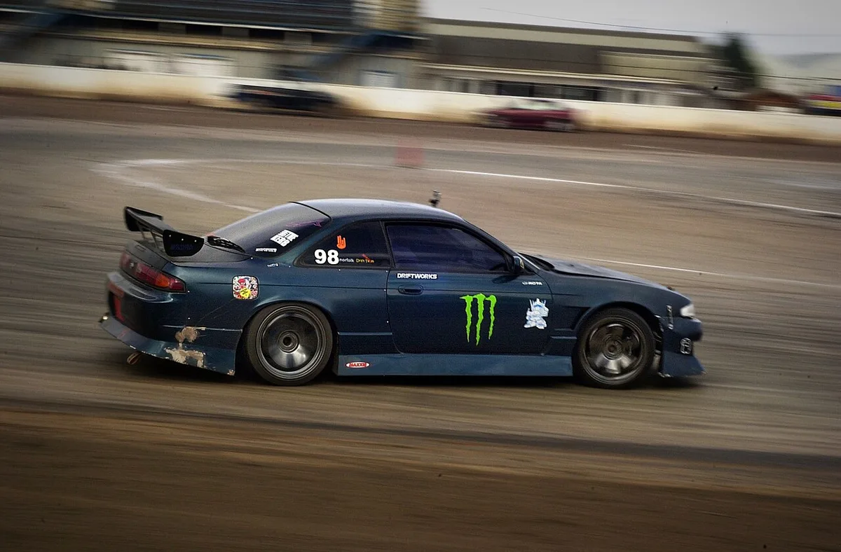 A Nissan S14 drifting at a grassroots event with a scuffed rear bumper