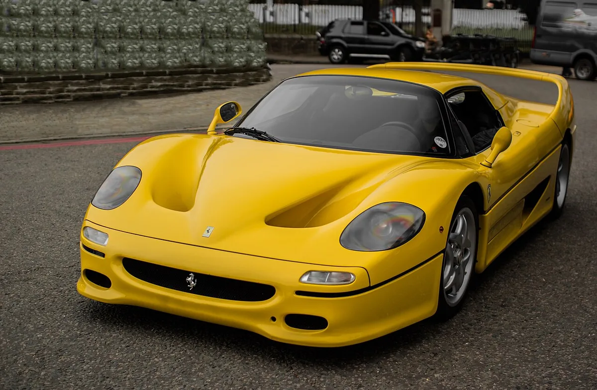 A yellow Ferrari F50 seen from the front three-quarter angle on a city street