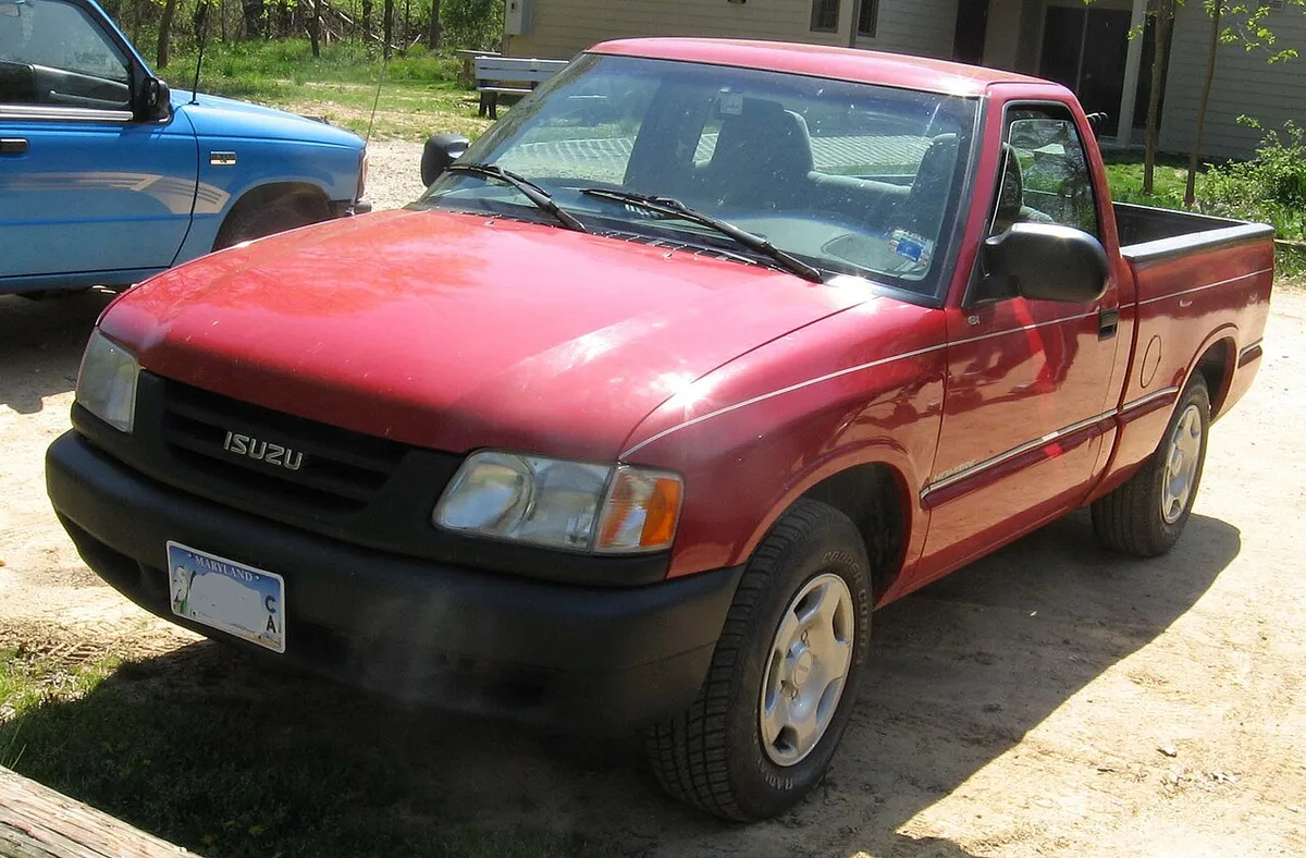A red 1996 or 1997 Isuzu Hombre regular cab pickup seen from the front three-quarter angle, showing its Isuzu grille and wraparound headlamps
