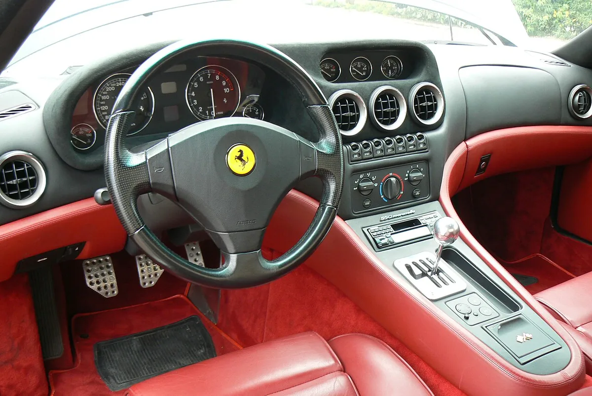 The interior of a Ferrari 550 Maranello with its gated six-speed manual shifter and red leather