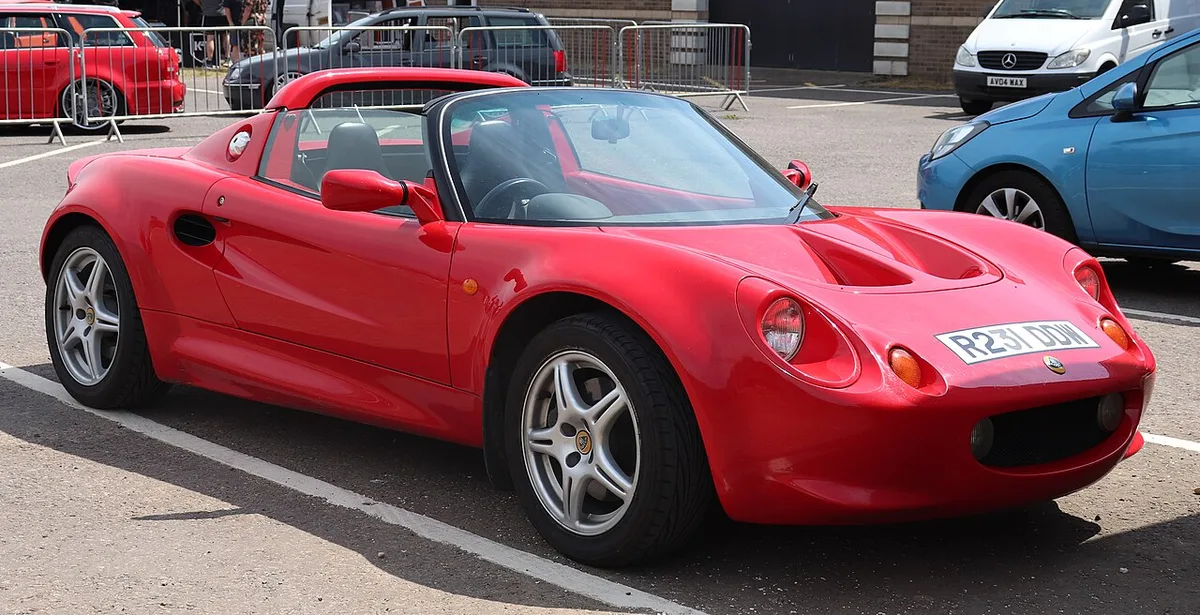 A red first-generation Lotus Elise with its roof off, seen from the front three-quarter in a parking lot