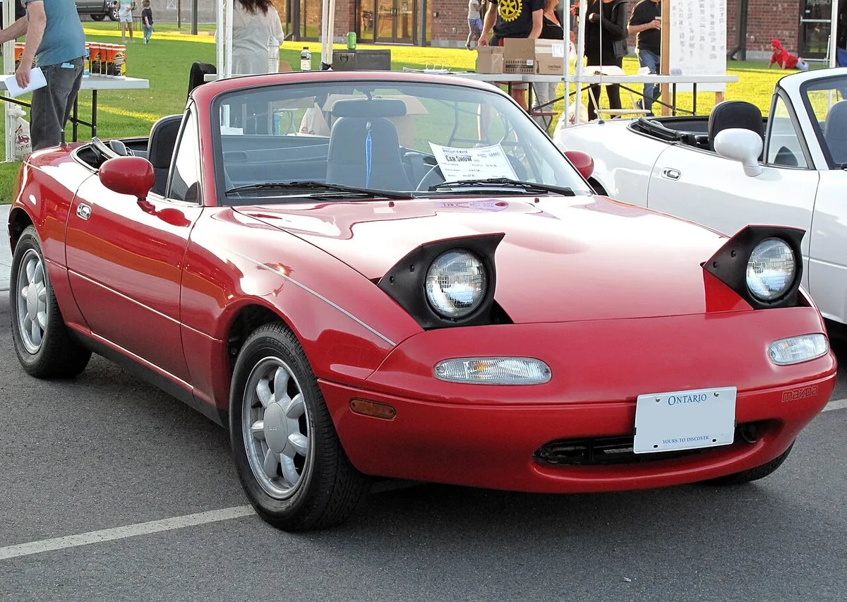 A 1991 Mazda MX-5 Miata in Classic Red with its headlights up
