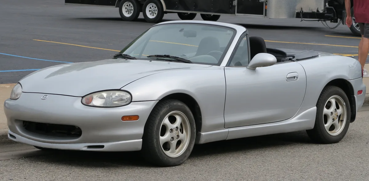 Silver 1999 Mazda MX-5 Miata NB showing the fixed headlights that replaced the pop-ups