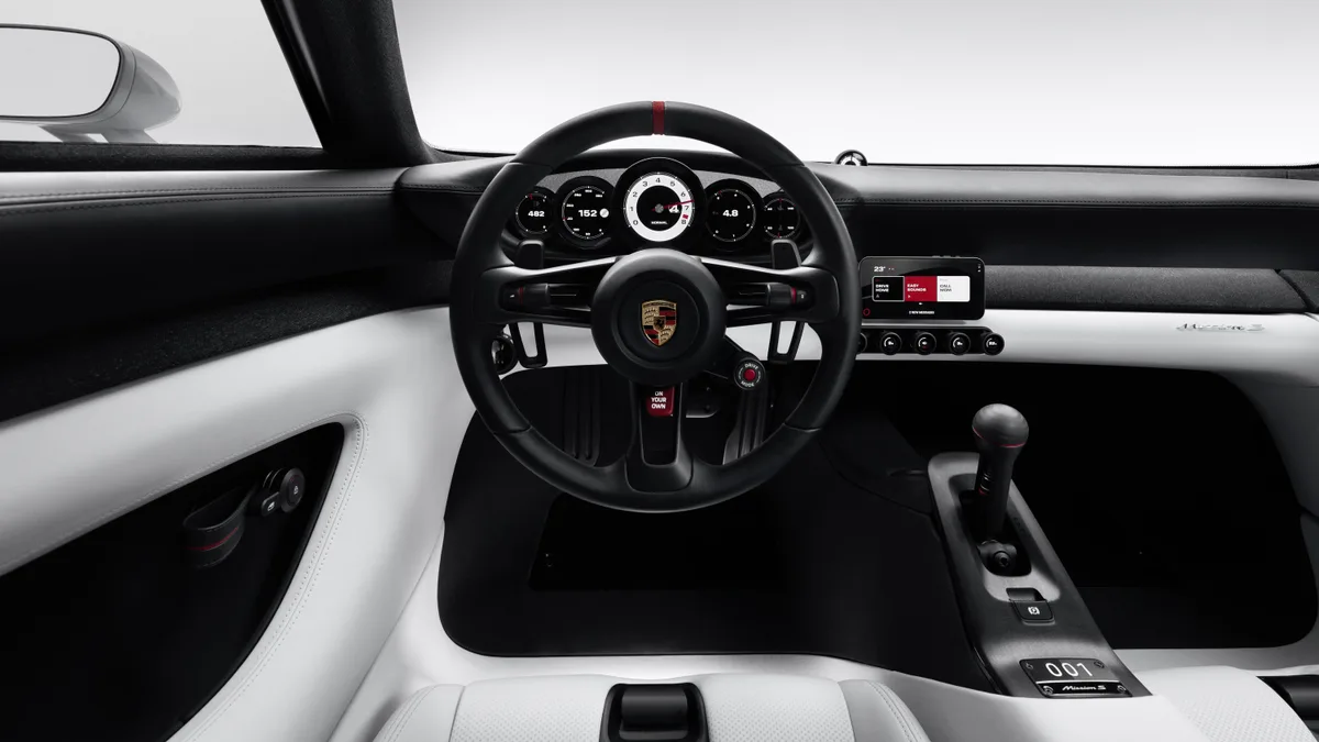 The Porsche Mission S cockpit, with five round gauges behind the steering wheel, a phone mounted on the dash above a row of knobs, and a tall gear lever