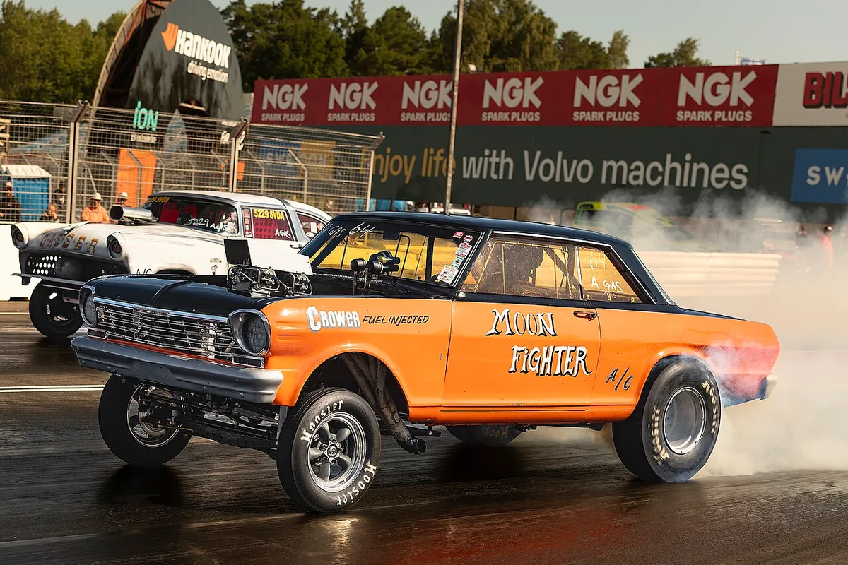 A Chevrolet Nova gasser launching at a drag strip with its nose up