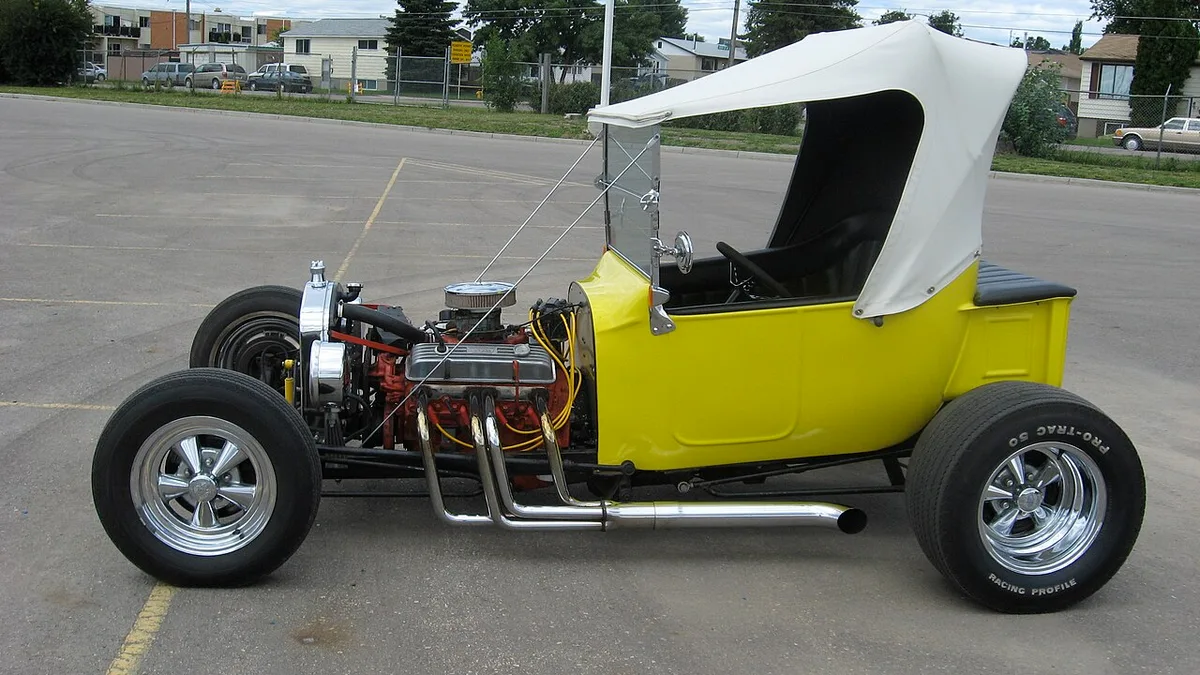 A yellow Ford T-bucket hot rod with big rear tires and small front tires