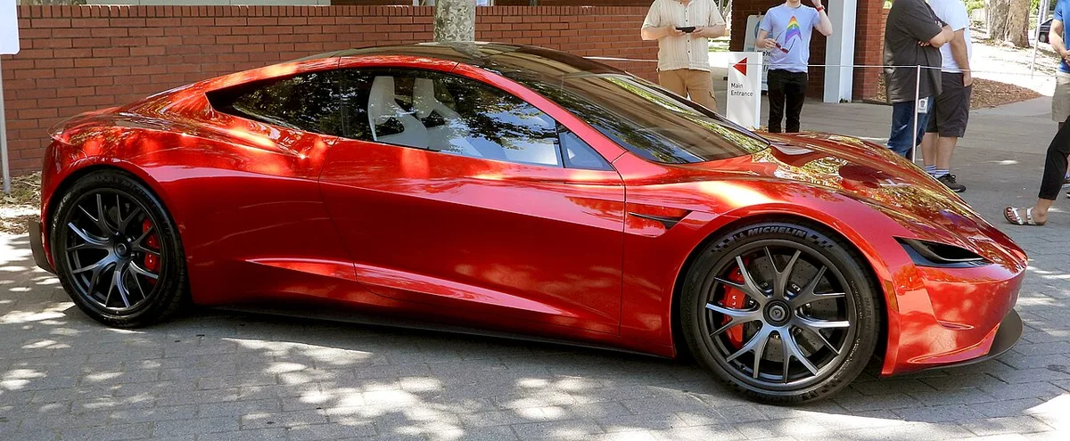 Side profile of a red second-generation Tesla Roadster prototype with rounded fenders and a long, curved roofline